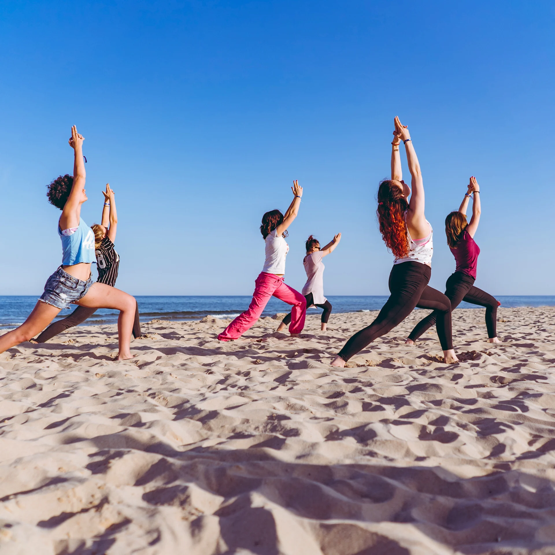 Yogagruppe bei einer stehenden Übung am Strand